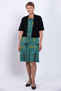 Woman in teal patterned dress layered with black short sleeve cardigan