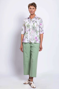 Three-quarter front view of a woman in a floral collar blouse and light green trousers
