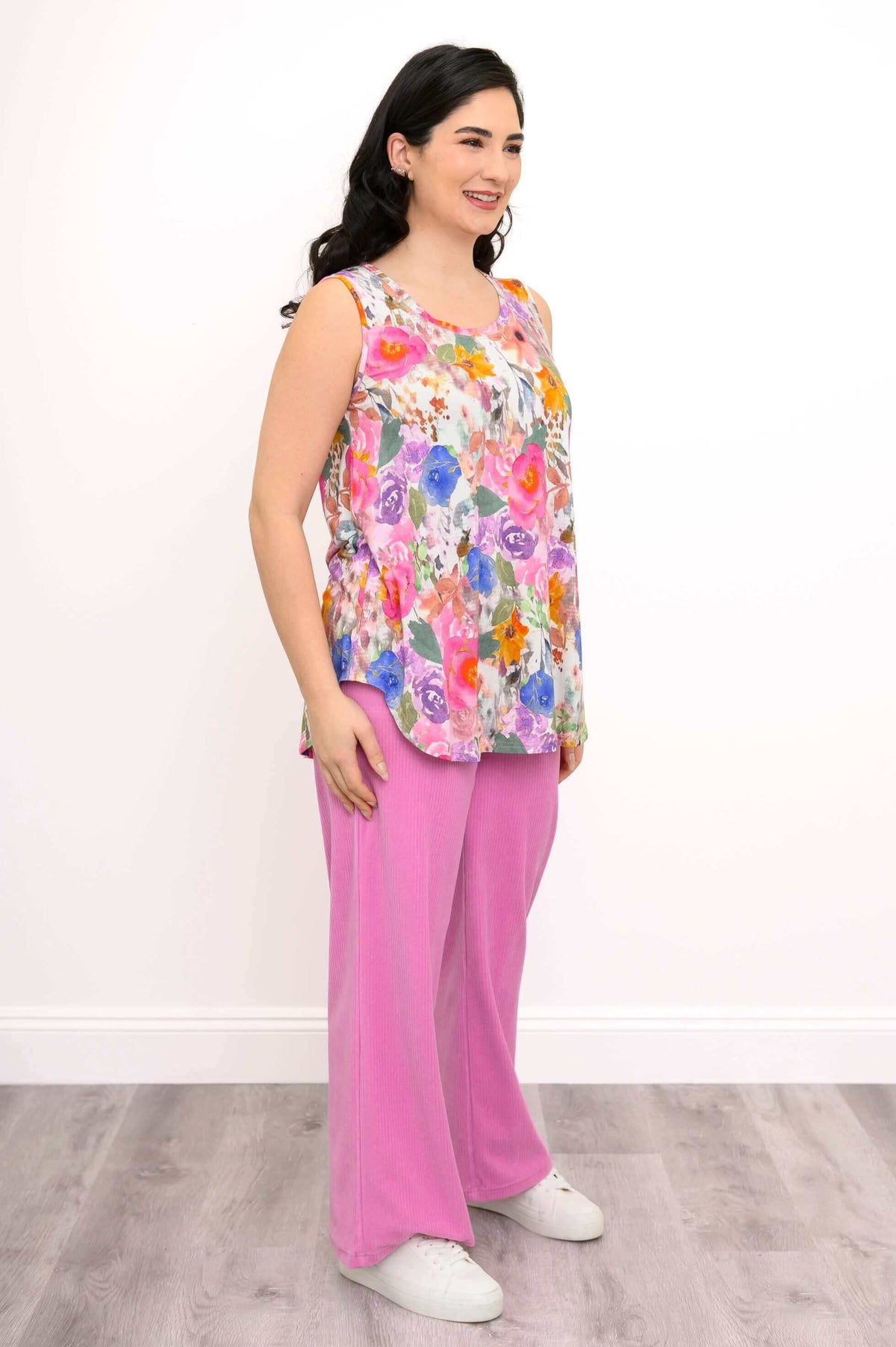 Three-quarter front view of woman smiling, wearing a full length pink floral tank, pink pants, and white shoes