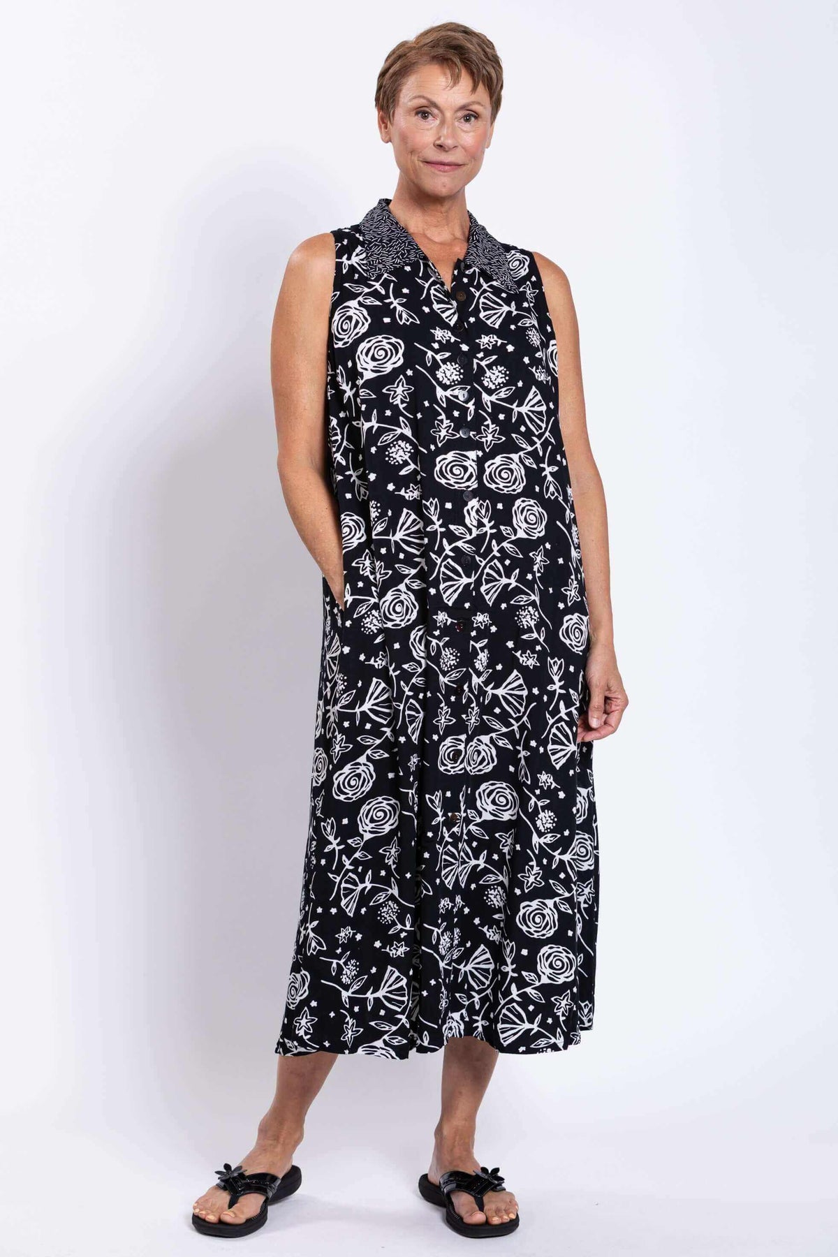 Three-quarter front view of woman in sleeveless floral black and white dress with pockets