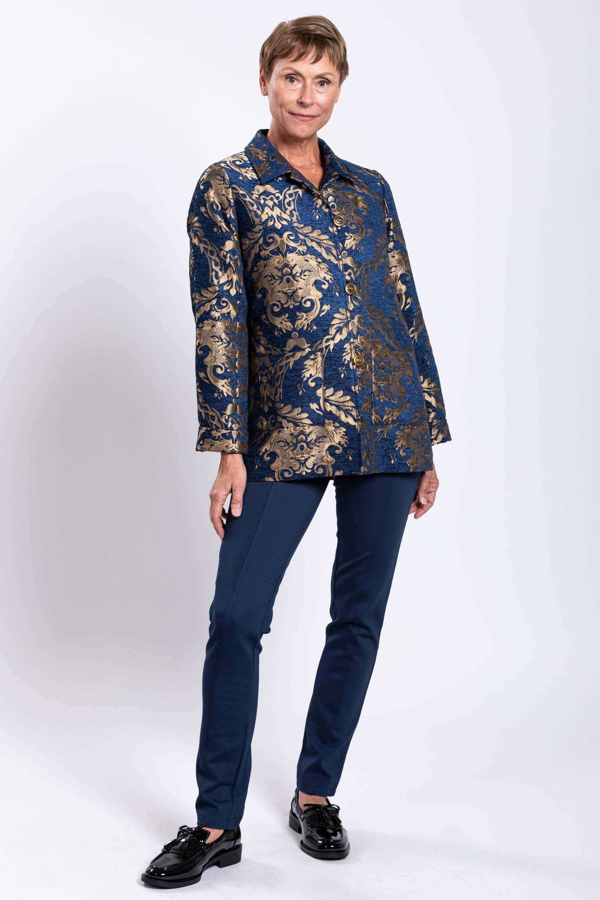 Three-quarter front pose of woman in blue and gold jacquard coat and navy pants