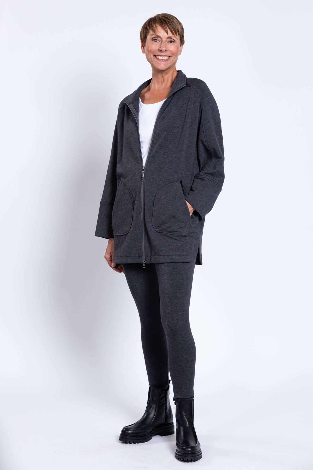 Three-quarter front view of woman modeling a charcoal grey jacket with pockets and zip closure