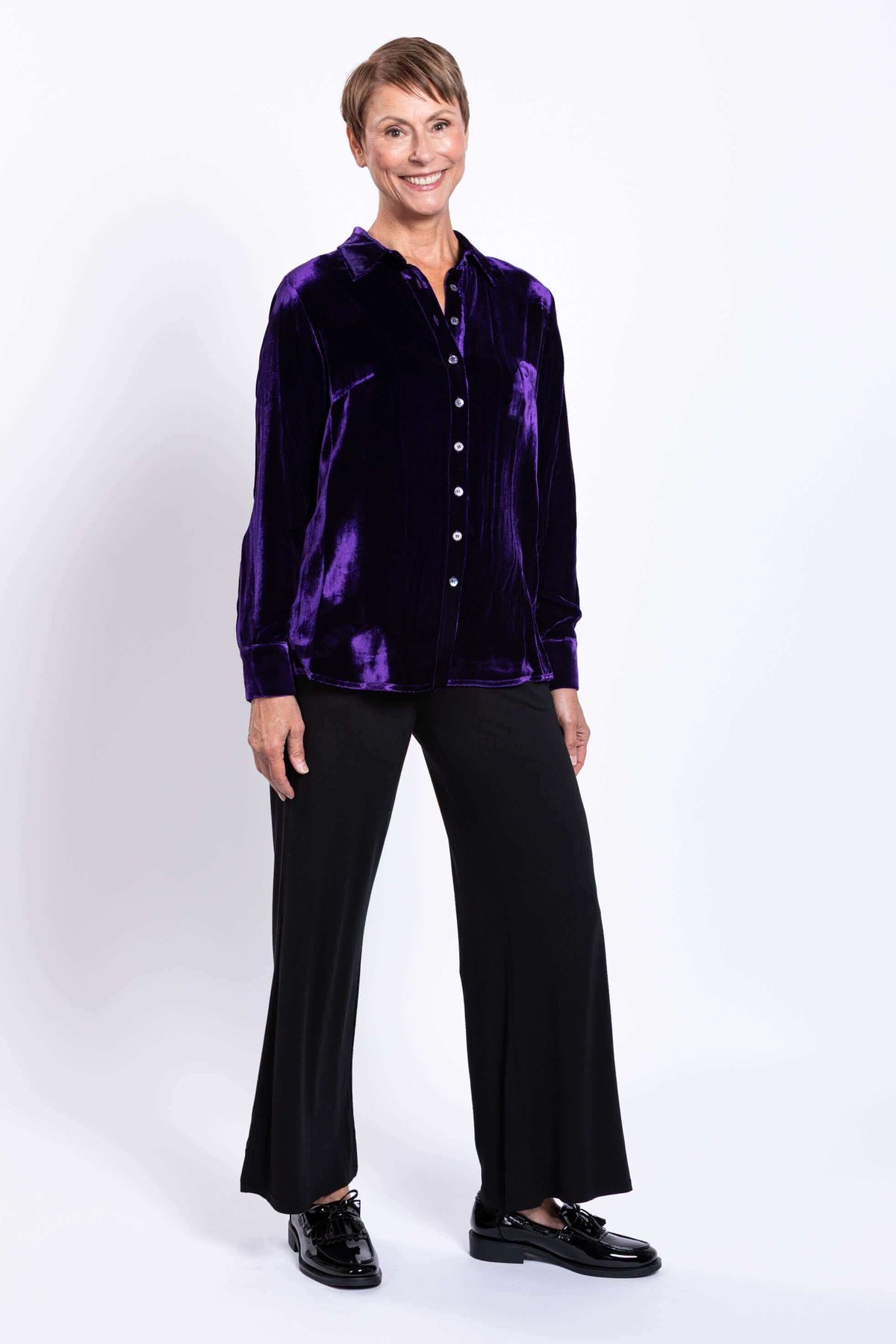 Woman in a deep purple velvet blouse and black pants, three-quarter front view