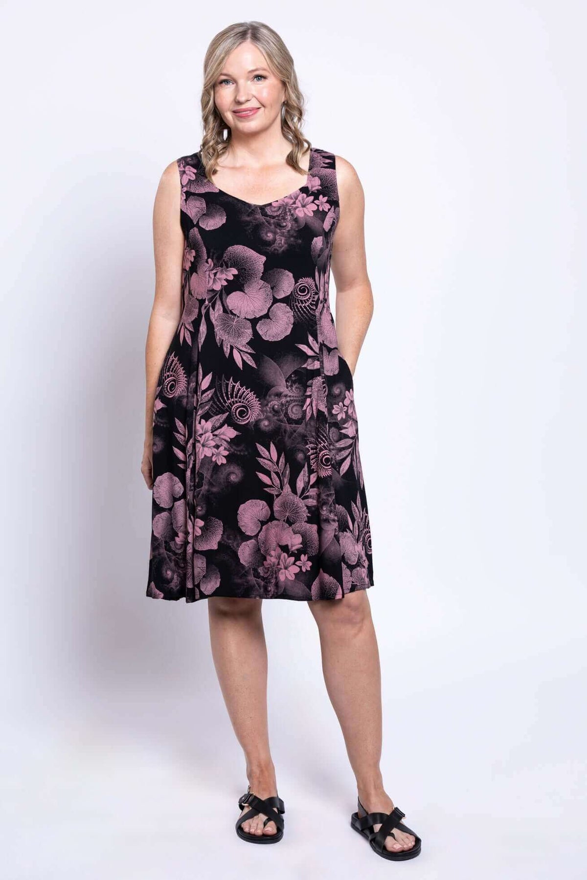 Three-quarter view of a woman modeling a sleeveless black A-line dress with pink floral print