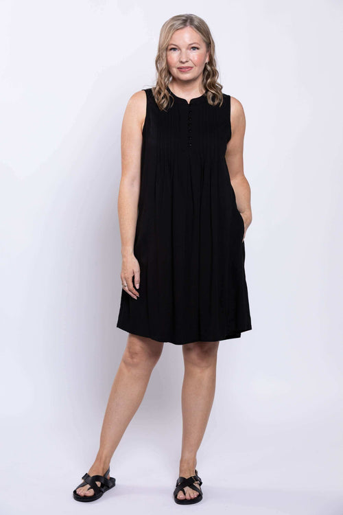 Three-quarter front view of woman in black sleeveless pintucked dress with hand in pocket