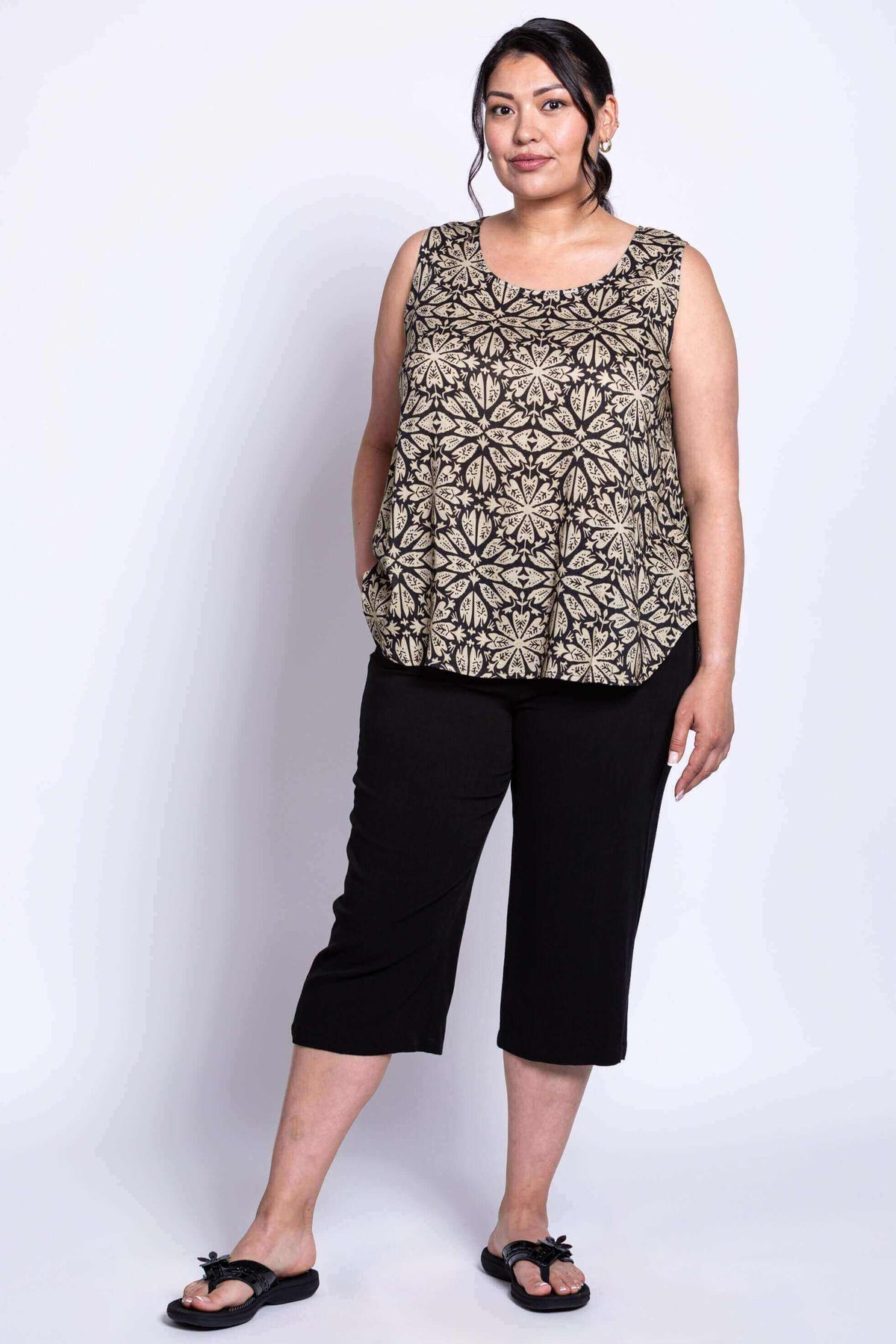 Three-quarter front view of model in black floral tank top with hands in pockets