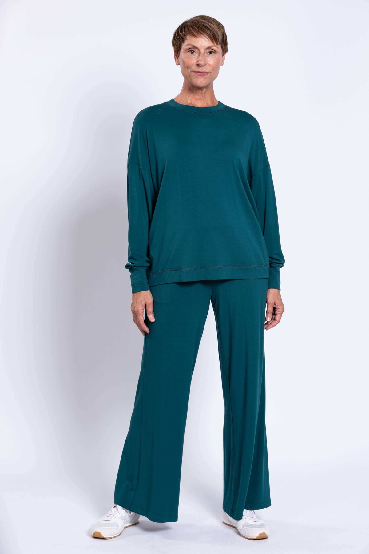Three-quarter front view of woman in teal relaxed fit crew neck top and matching pants