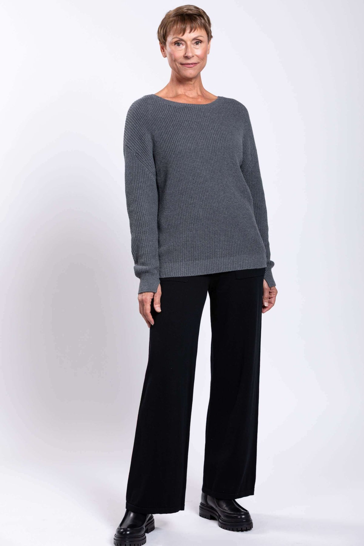 Three-quarter front view of woman in grey sweater and black wide-leg pants
