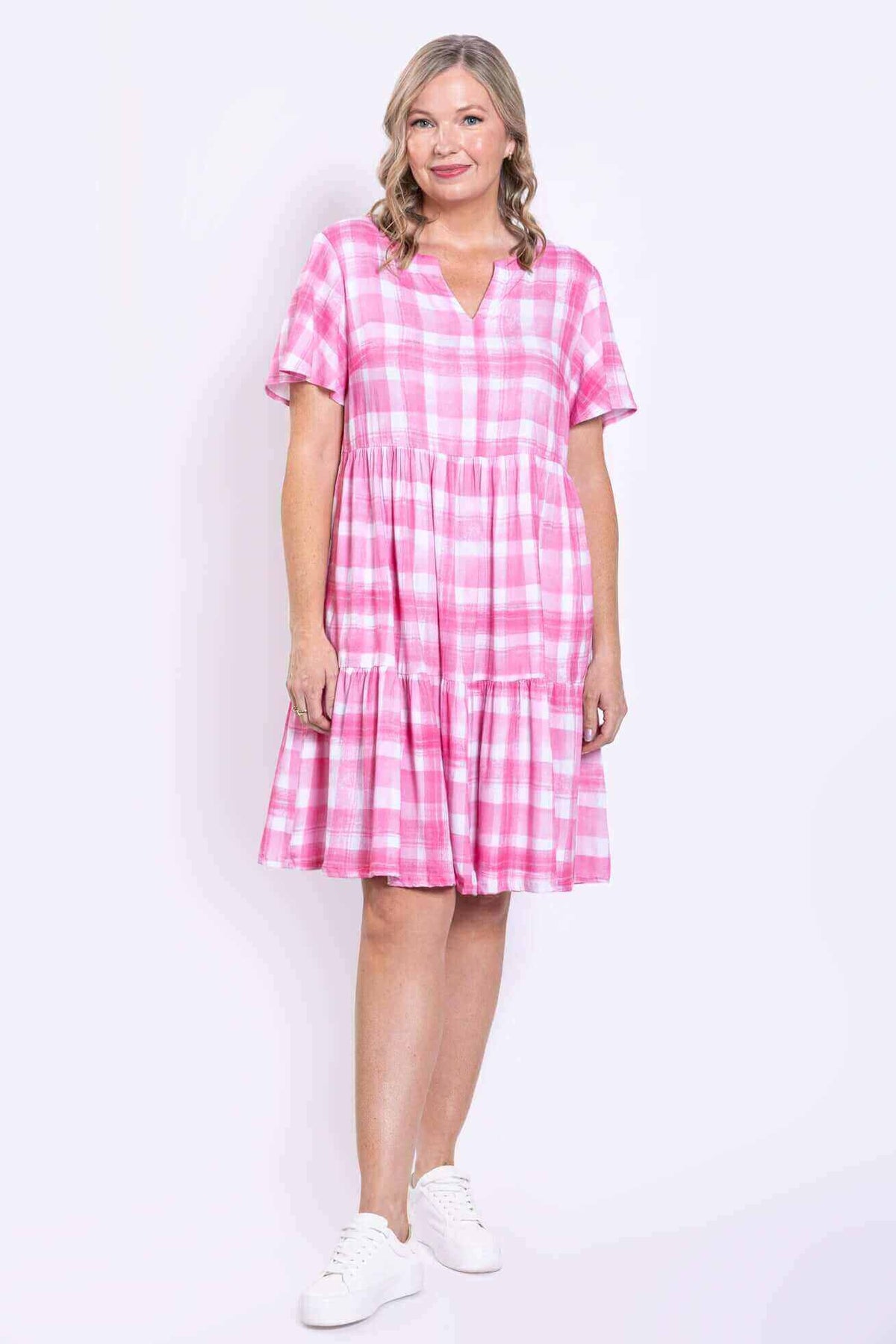 Woman in pink check dress with pockets and short sleeves standing three-quarters to camera