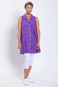 Three-quarter view of woman in violet patterned button up tank top over white leggings
