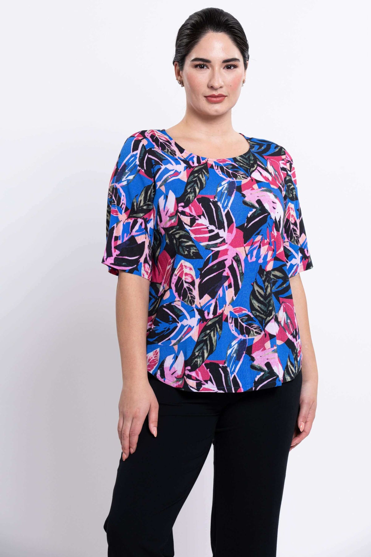 Three-quarter front view of woman wearing round-neck blouse in blue and pink leaf print