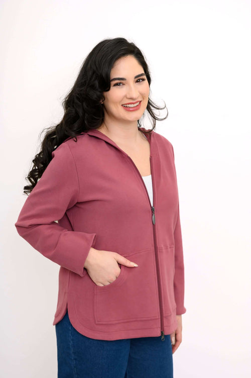 Three-quarter view of a woman in a rose-colored zip hoodie jacket with her hand in the pocket