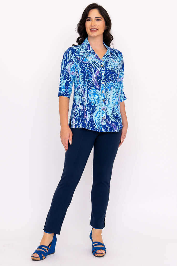 Woman modeling blue patterned blouse and navy pants, looking to the side