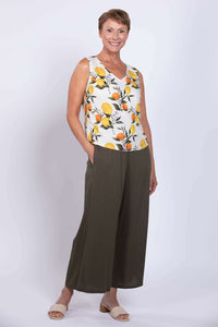 Three-quarter view of woman standing in lemon print sleeveless V-neck tank with olive pants
