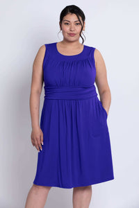 Model in royal blue ruched dress standing with hand in pocket, three-quarter view