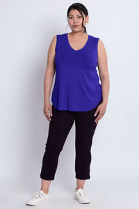 Three-quarter front view of woman in royal blue sleeveless V-neck tank top and black pants.