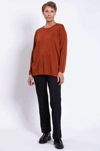 Three-quarter angle of woman in rust Merino sweater and black trousers