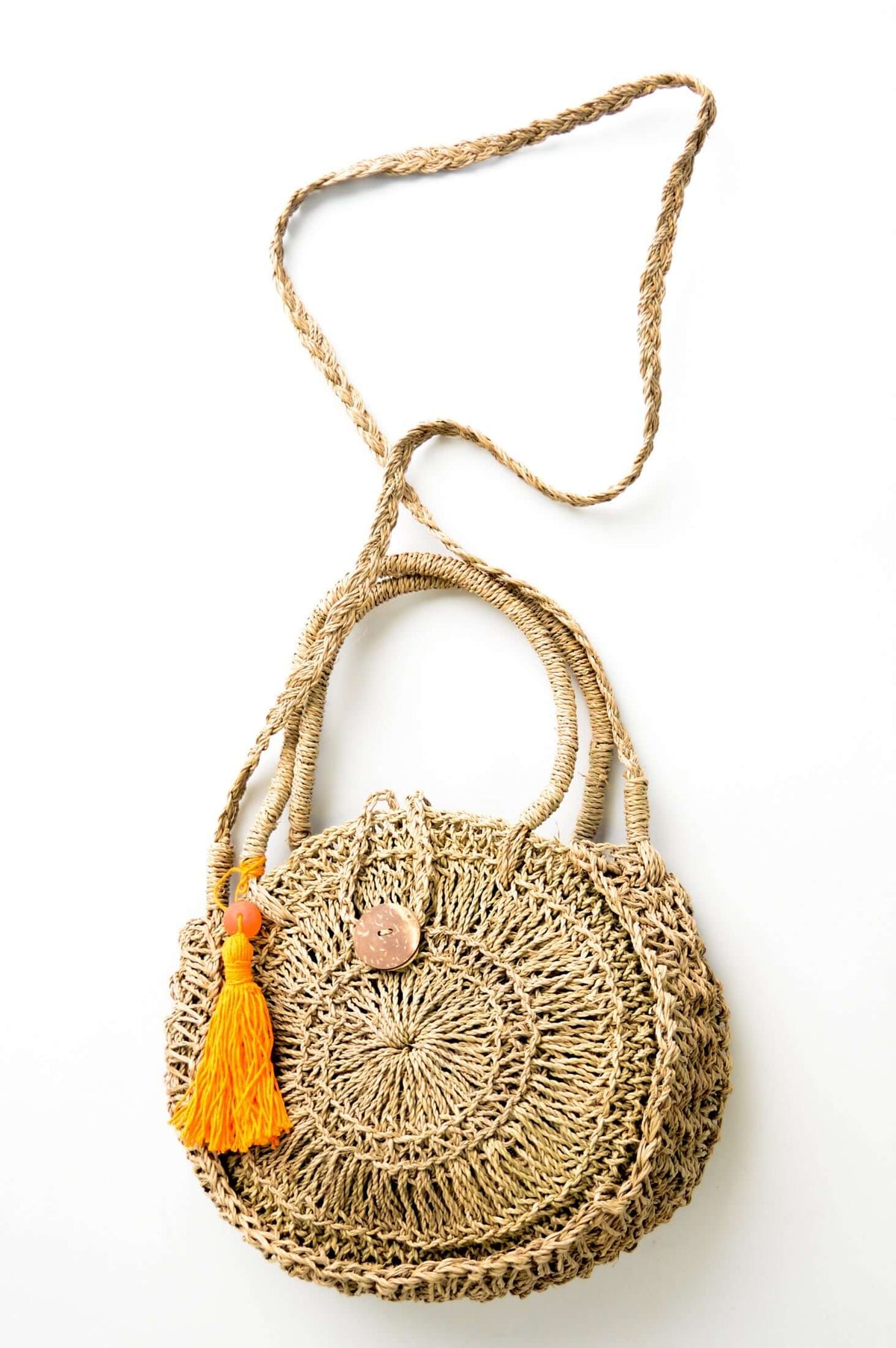 Top view of hand woven rattan bag with orange pom-pom and extended braided shoulder strap