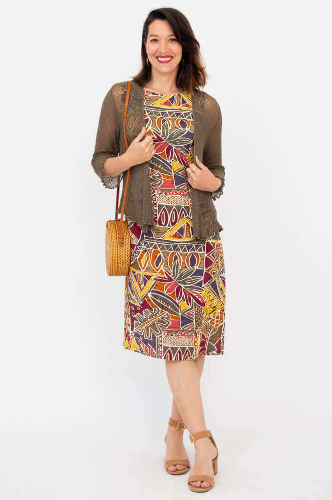Woman in abstract print dress with sheer brown cardigan and woven bag, posing