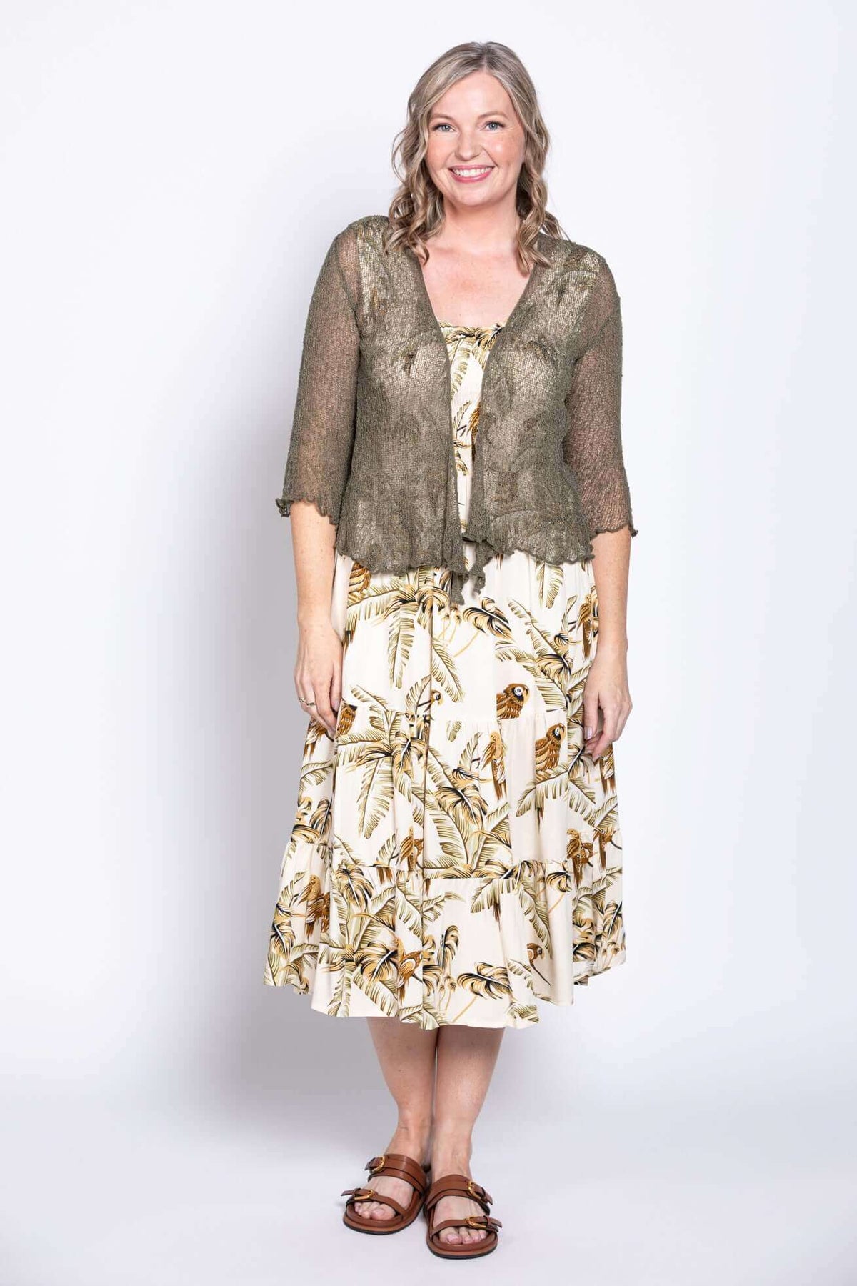 Woman in tropical print dress and olive cardigan smiling at camera