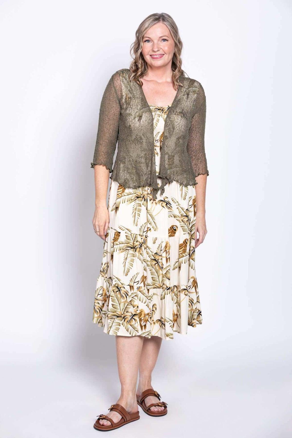 Woman in cream tropical print dress paired with a sheer olive cardigan