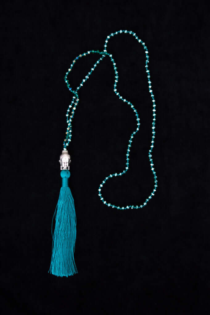 Turquoise beaded mala necklace with silver Buddha and long tassel on black background