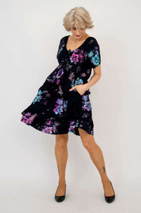 Model twirling in a short-sleeve black dress with purple and blue floral print