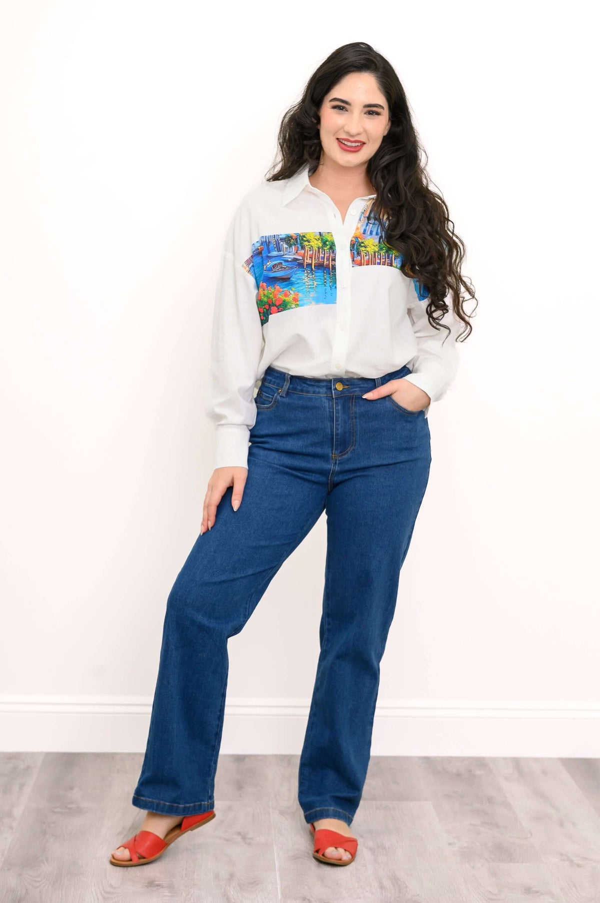 Woman in full-length shot wearing Venice print blouse with jeans and red sandals
