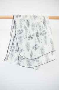 A large silk scarf with a black and white leaf pattern displayed on a wooden rod against a white wall, front view
