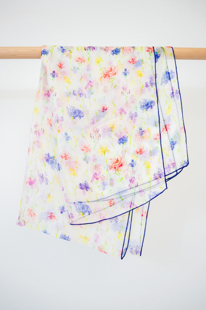 A large silk scarf with a multicolor floral print displayed on a wooden rod against a white background, front view