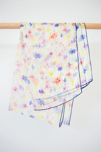 A large silk scarf with a multicolor floral print displayed on a wooden rod against a white background, front view