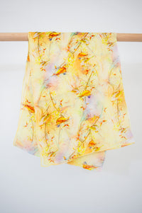 A yellow and multicolored large silk scarf with a bird pattern displayed on a white background, front view