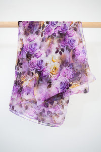 A large silk scarf with a purple floral print on a wooden rod against a white background, front view