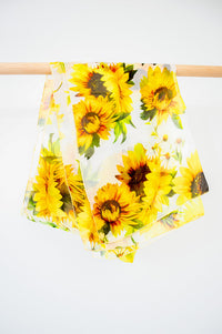 A large silk scarf with a sunflower pattern displayed on a white background, front view