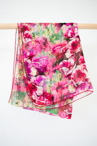 A large silk scarf with a pink and green floral pattern displayed on a wooden rod, front view