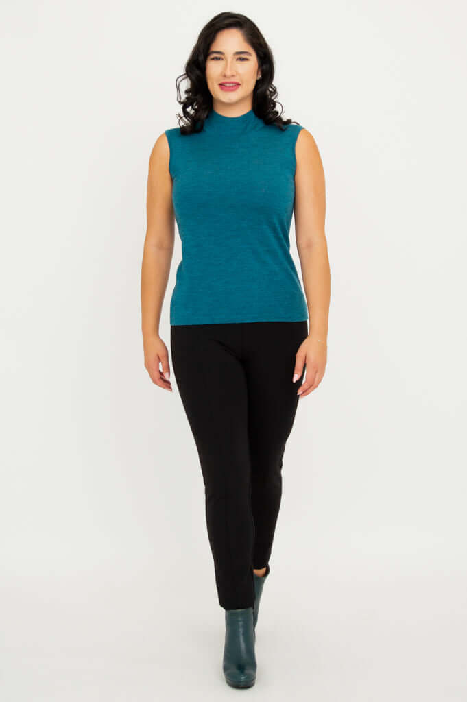 Woman walking forward in teal merino wool sleeveless mock neck sweater and black pants
