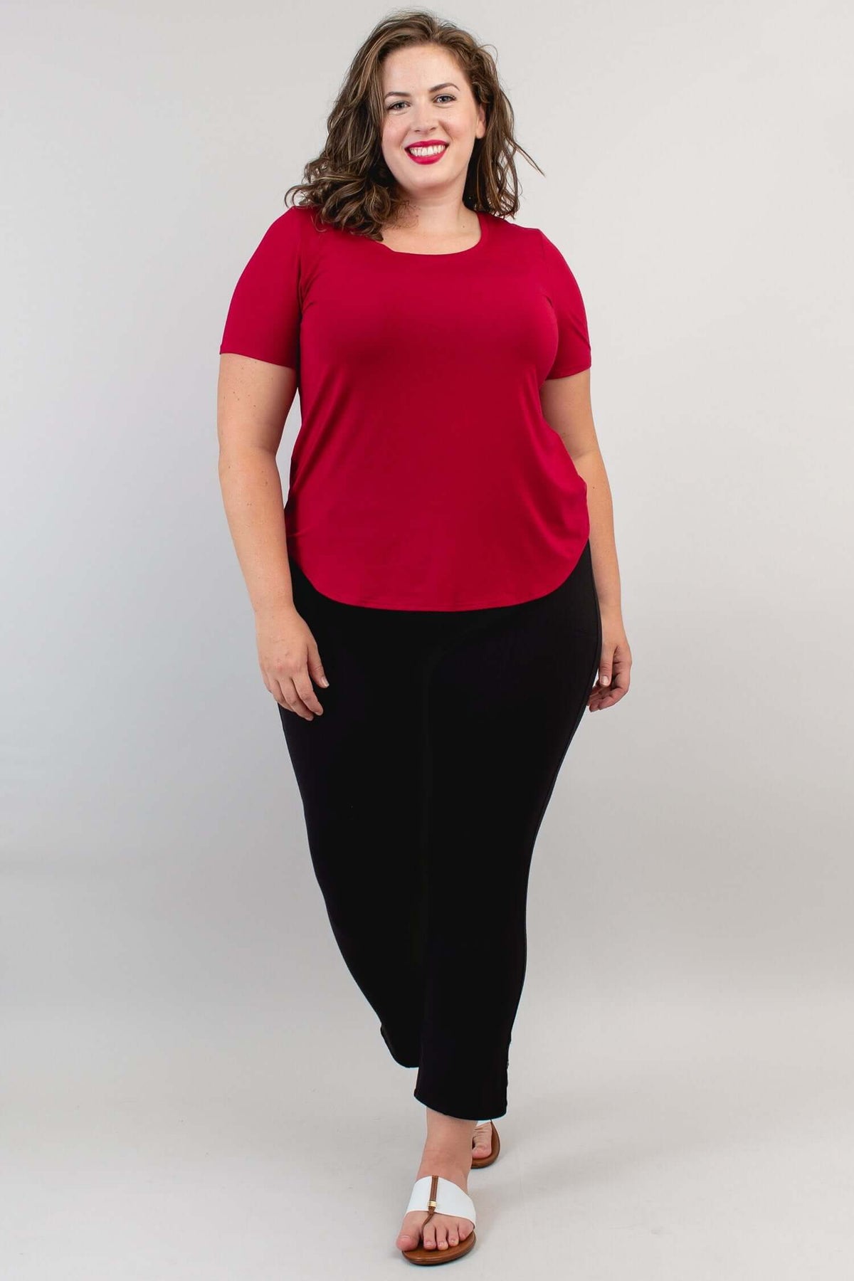 Woman walking in a crimson scoop neck tee and black pants, full body, front view