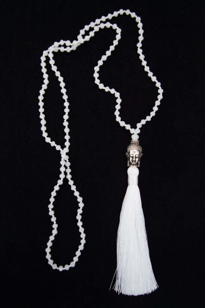 White beaded mala necklace with a silver Buddha pendant and long white tassel on a black background