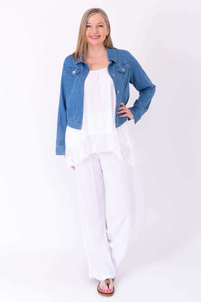 Woman layered in a white lace tank top and blue denim jacket, hands on hip