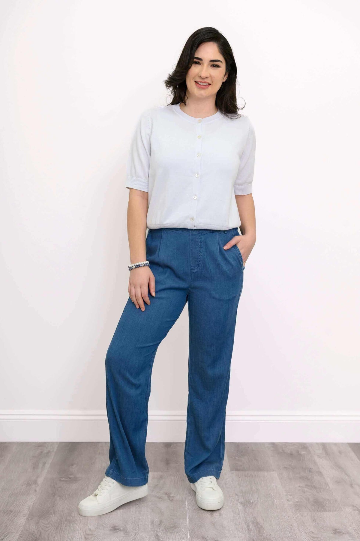 Model in a short-sleeve white cardigan and blue pants, standing confidently