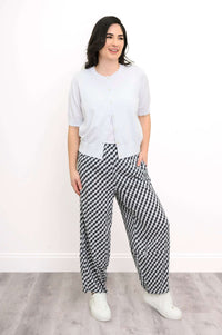 Model wearing a white cardigan and checkered pants, standing and smiling