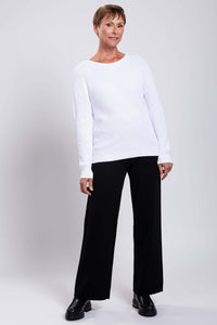Model in a white cotton sweater and black pants standing with one hip tilted