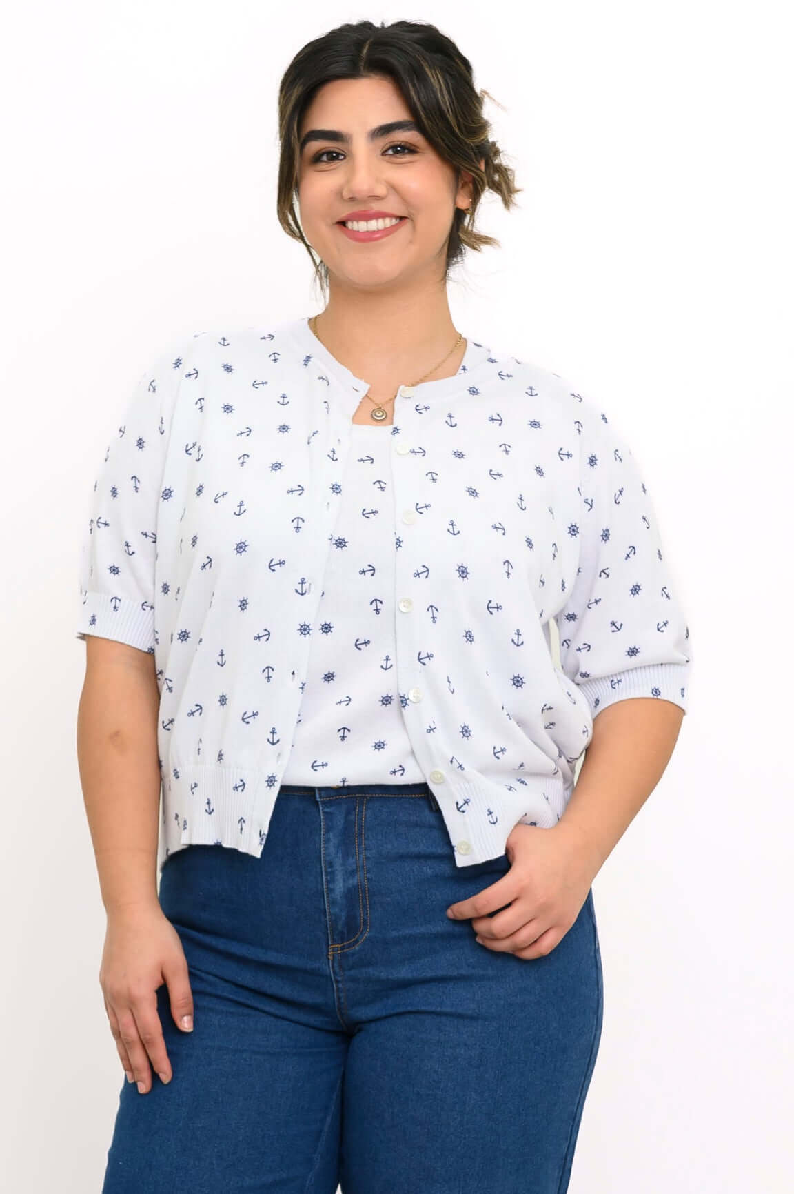 Woman wearing a white short sleeve cardigan with navy nautical motifs and blue jeans