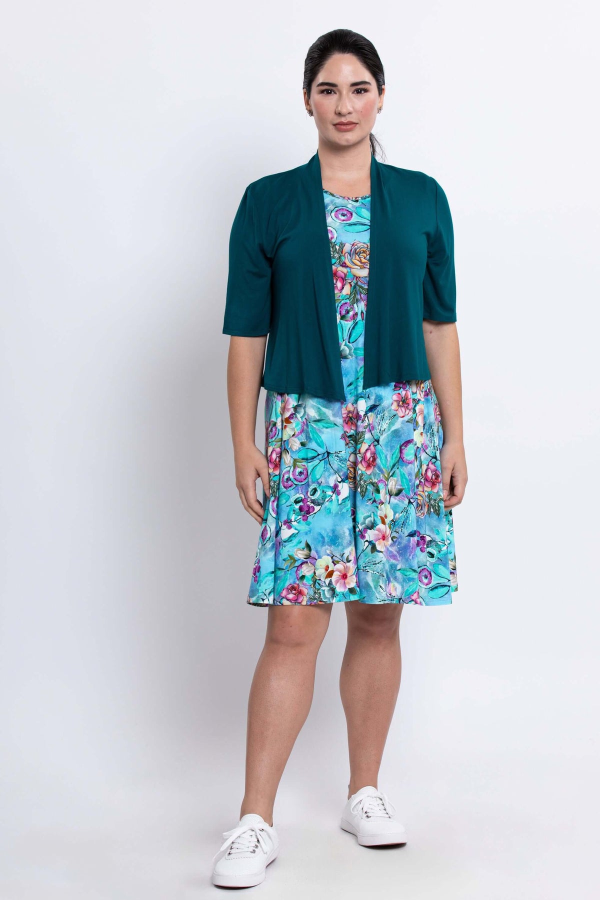 Woman modeling a blue floral dress with a teal cardigan and white sneakers