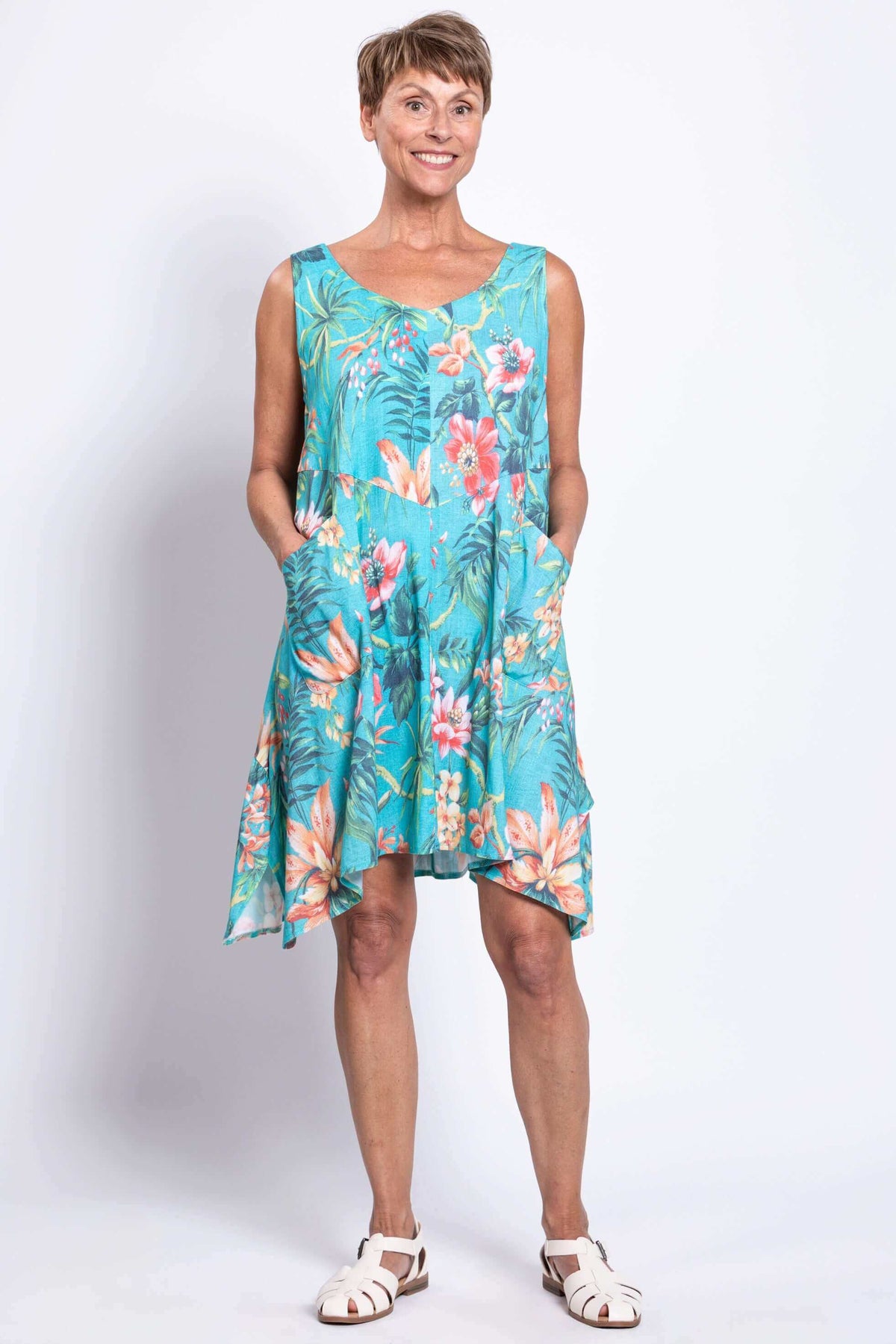 Woman wearing a turquoise sleeveless dress with vibrant tropical floral print, hands in pockets