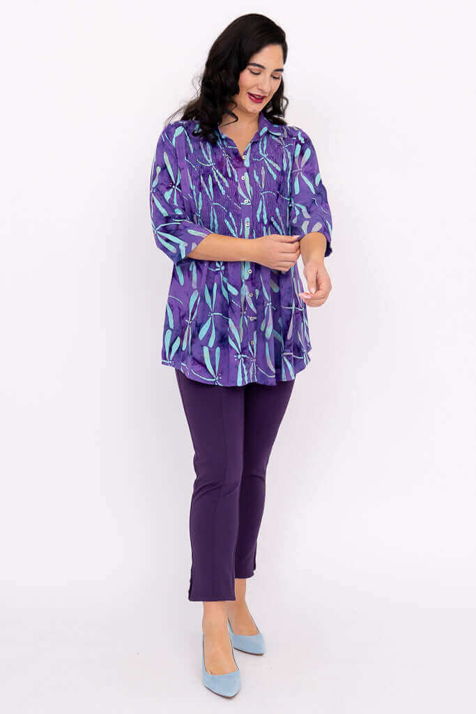 Woman adjusting sleeve of Cindy dragonfly violet tunic, wearing violet pants and blue heels