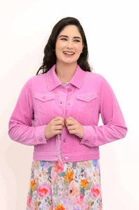 Smiling woman fastening buttons on a pink corduroy jacket over floral dress