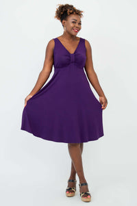 Woman displaying the flowy skirt of a sleeveless purple dress by spreading the hem