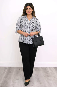 Woman dressed in a floral blouse with black pants, holding a black handbag