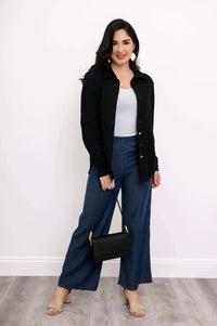 Woman in black button-up shirt, white top, blue pants, and holding a black handbag
